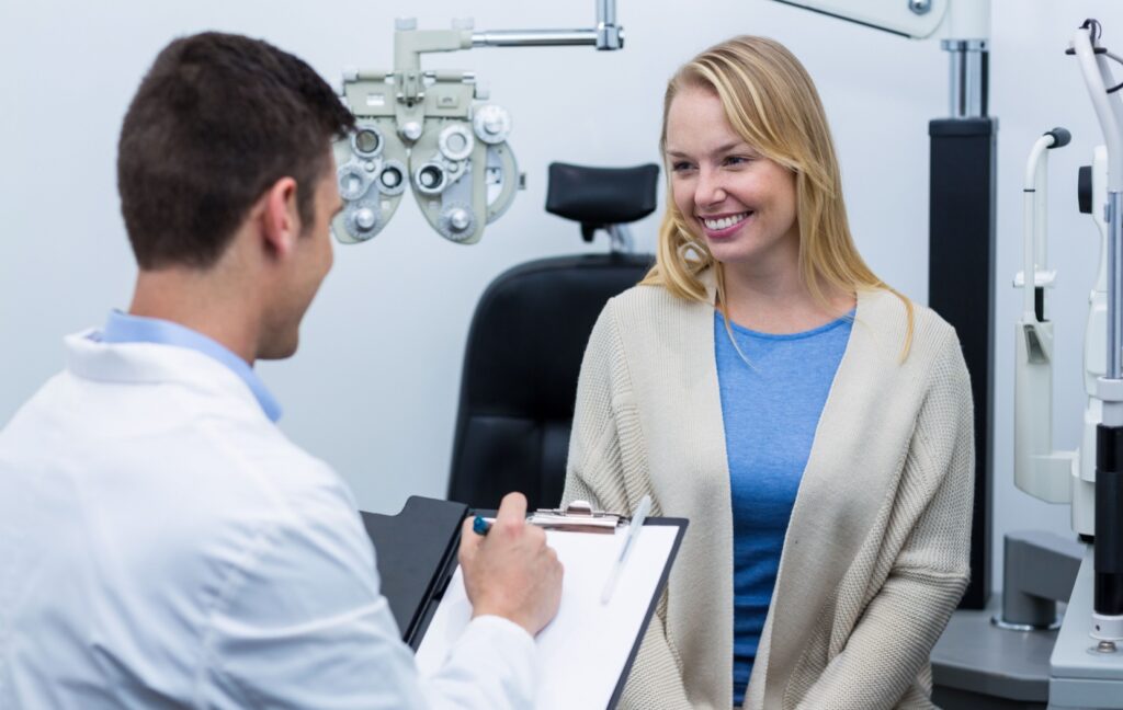 An optometrist explains the results of an eye exam to their patient while sitting in the optometrist's office.