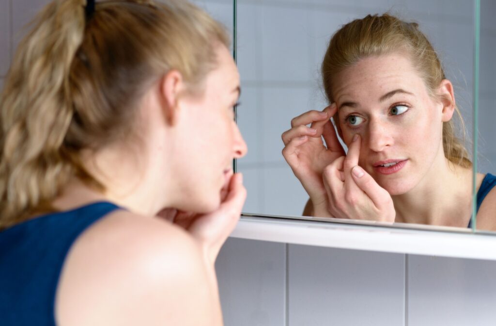 A young adult carefully looking for a stuck contact lens in their eye using their bathroom mirror.