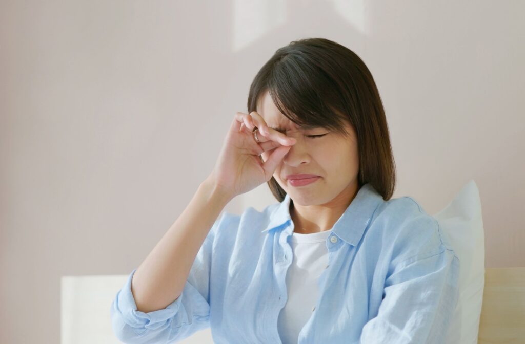 A person wakes up in bed and rubs their dry, irritated eyes.