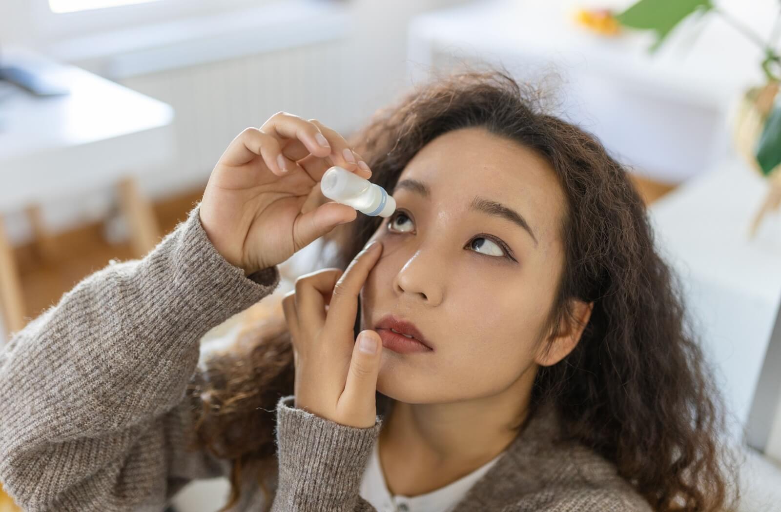 A person carefully pulls down their eyelid and applies eye drops to treat their dry eye.