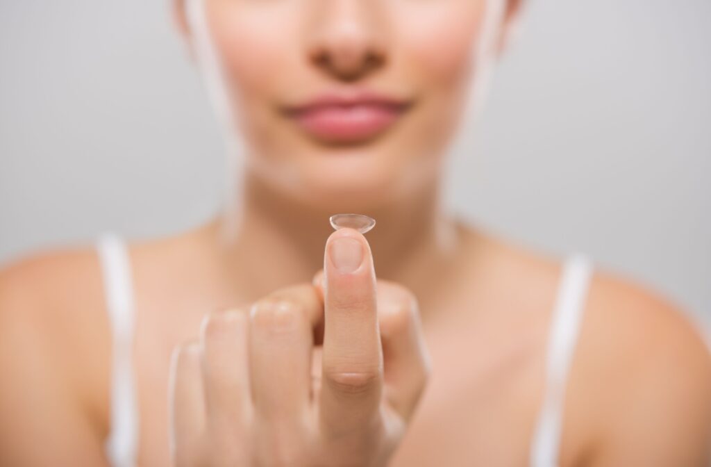 A person wearing a white shirt holds a clean contact lens up in front of them on their finger.