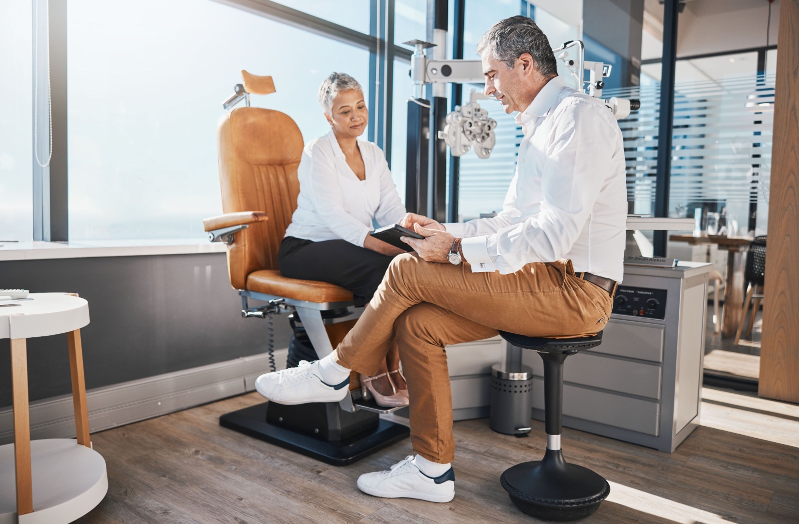 A patient sitting across from an optometrist in an exam room after an eye check-up, both reviewing results.
