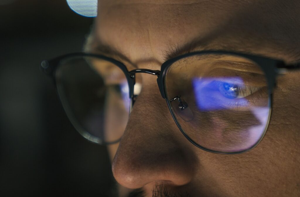 Close-up of a person experiencing dry eyes while wearing glasses in front of a computer.
